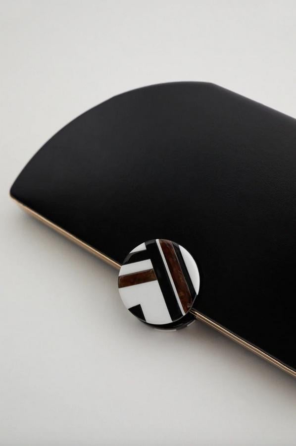 Con cuerpo ovalado con contorno metalizado, este bolso en formato caja y color negro de Zara viene con asa de hombro con cadena para convertirse en bandolera y su bonito cierre de imán es circular con estampado geométrico. Tiene un precio de 35,95 euros.