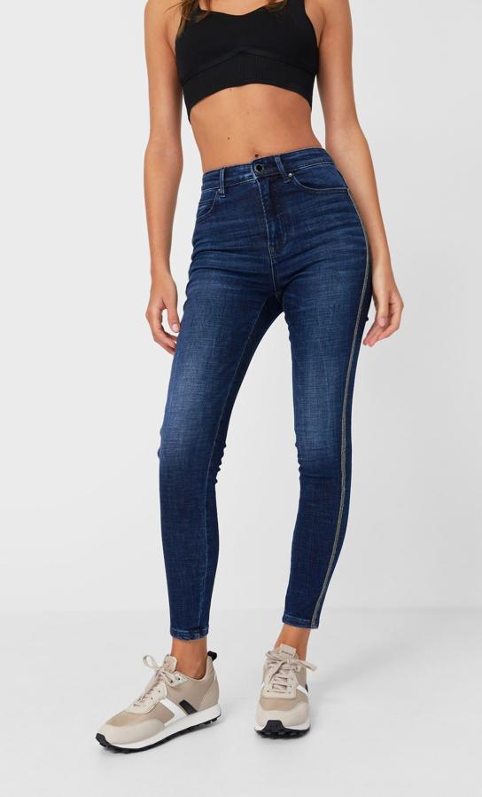 Diseño ajustado y tiro alto para estos vaqueros en denim medio de efecto lacado con cierre frontal de cremallera y botón metálico y detalle de bandas laterales con brillo en cada pernera. Tienen un precio de 25,99 euros y están disponibles entre las tallas 32 y 44.