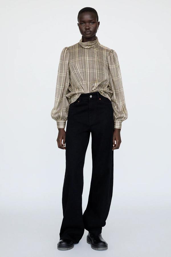 Esta blusa con cuadros en varios tonos con hilo metalizado cuenta con cuello subido y cierre con botones metálicos en los hombros. Es de Zara y tiene un precio de 25,95 euros.