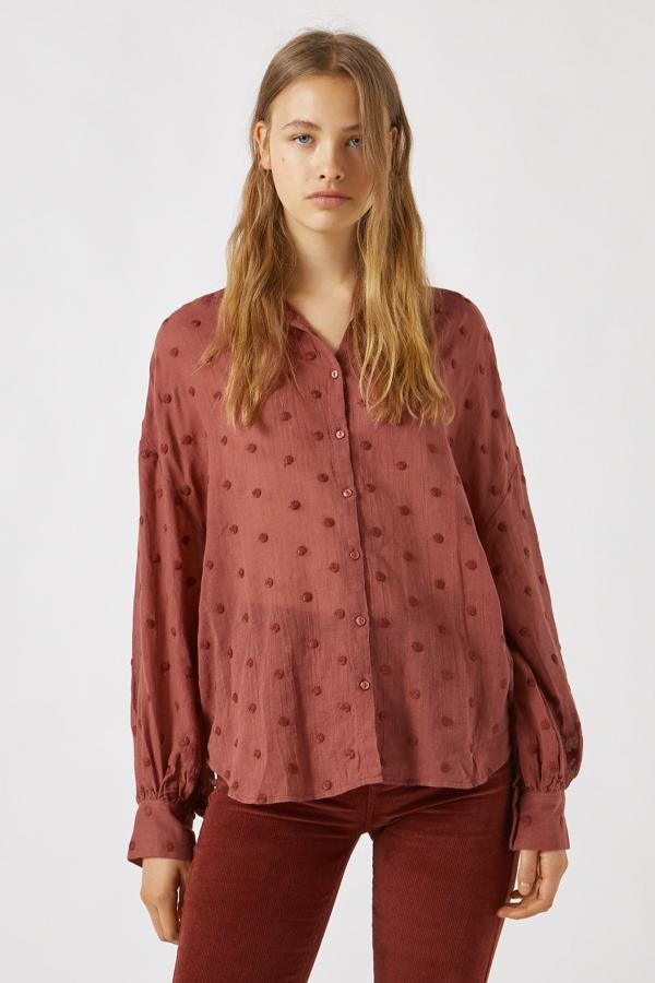 Esta camisa en tejido de plumeti de color teja está confeccionado en algodón y cuenta con cierre mediante botones. Disponible también en negro, tiene un precio de 19,99 euros.