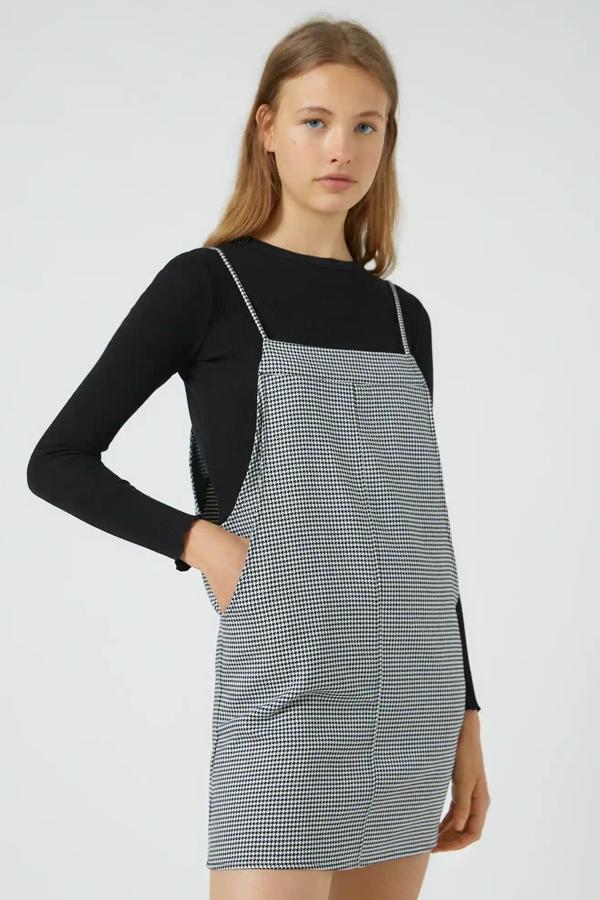 En color negro o marrón, este vestido de cuadros con detalle de bolsillo delantero y tirantes cuenta con escote recto y está confeccionado en tejido ligeramente elástico. Es de Pull & Bear y tiene un precio de 22,99 euros.