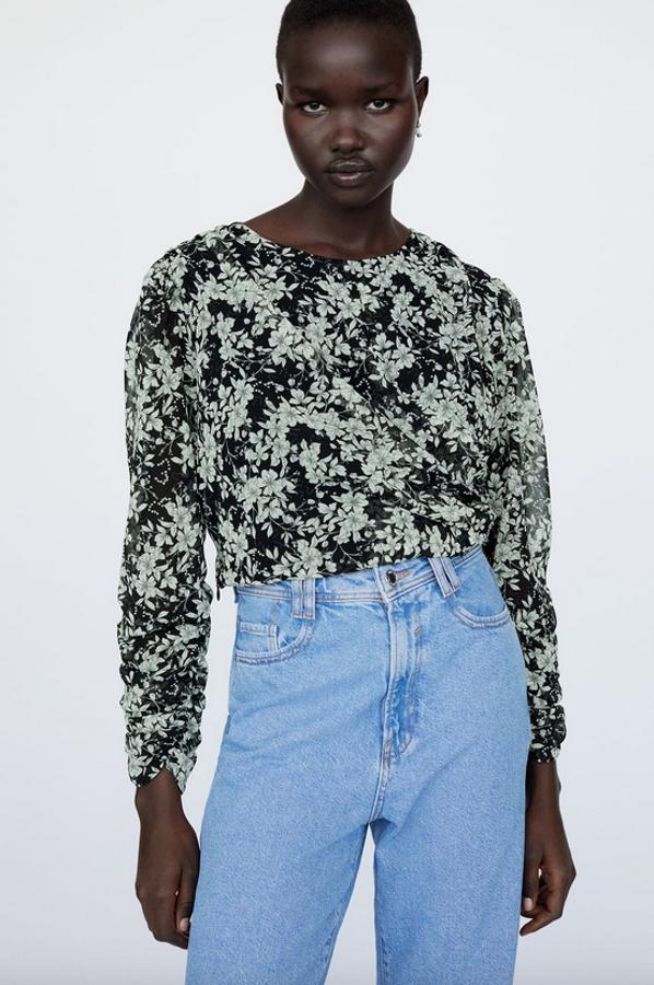 Con cuello redondo y manga larga acabada en frunces elásticos, esta blusa cropped de Zara con estampado de flores blancas sobre fondo negro viene con bajo acabado con frunces laterales. Disponible entre las tallas XS y L, cuesta 25,95 euros.