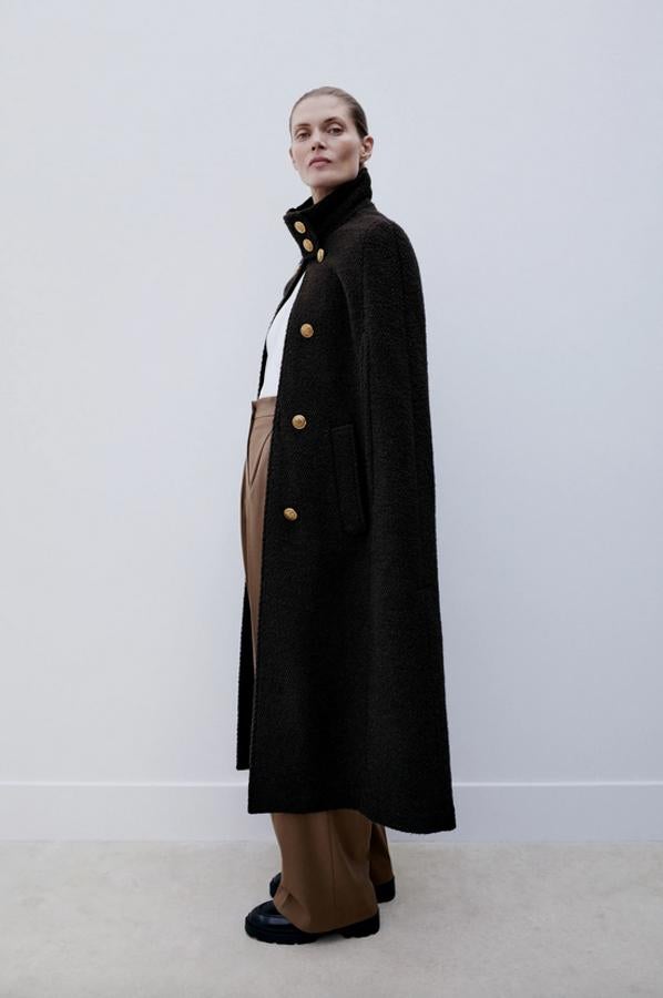 Con detalle de falsos botones metálicos en el frontal, esta capa negra larga de Zara está confeccionada en tejido con mezcla de lana y tiene bolsillos en delantero. Con cierre de ganchos metálicos, cuesta 109 euros y está disponible en las tallas XS-S y M-L.