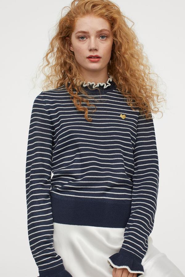 En color azul oscuro con finas rayas en blanco, este jersey en punto fino de H&M cuenta con detalle de bordado en el pecho y ribete de canalé con volante en el cuello y en los puños. Tiene un precio de 24,99 euros.