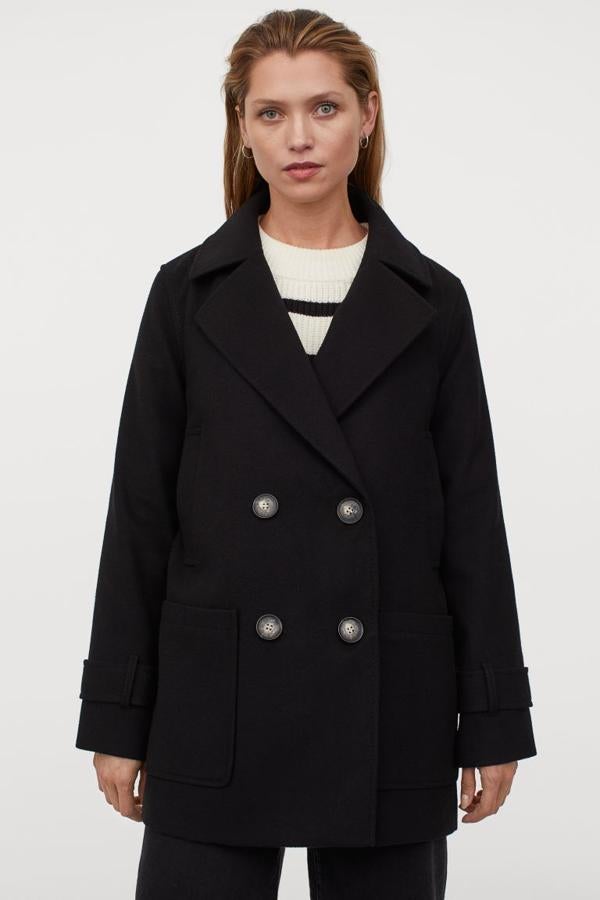 Diseño corto de doble botonadura para este abrigo negro de H&M con solapas de muesca y trabilla en los puños. Con bolsillos de plastrón en el frontal y abertura detrás, tiene un precio de 49,99 euros y está disponible entre las tallas XS y L y en la XXL.