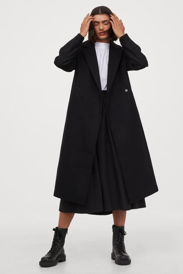 Con solapas de muesca, frente cruzado con botones de presión ocultos y cinturón de anudar extraíble a tono, este abrigo negro de H&M, que también podemos encontrar en camel, viene con bolsillos al bies discretos y abertura detrás. Tiene un precio de 49,99 euros y está disponible entre las tallas 32 y 40.