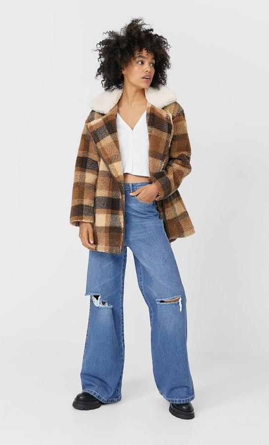 Con cuello a contraste, este abrigo corto con estampado de cuadros en tonos beige y marrón está confeccionado en borreguito y viene con cierre de cremallera frontal. Tiene un precio de 49,99 euros y está disponible entre las tallas XS y XL.