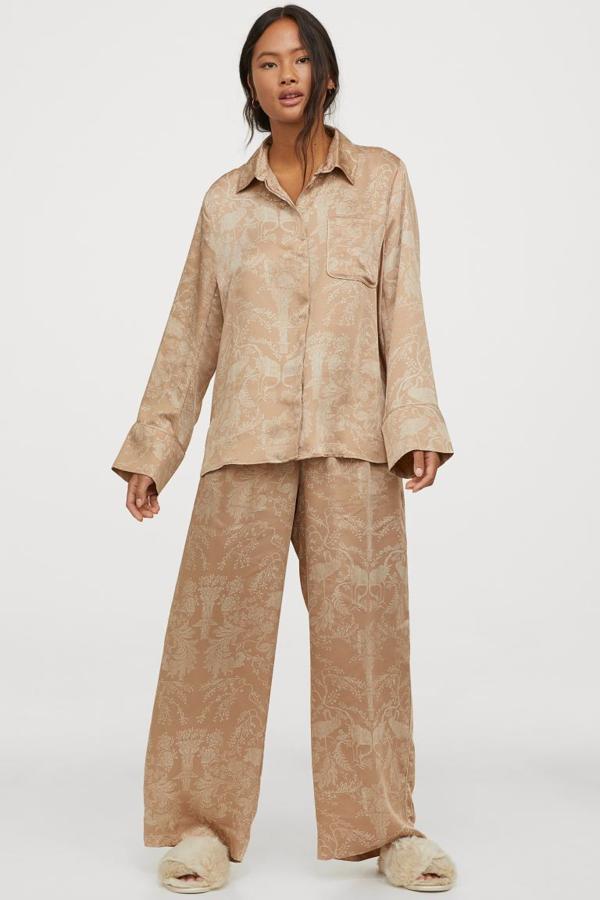 Disponible en beige empolvado con estampado tropical o en color negro liso, este pijama de satén de H&M con camisa de manga larga con cuello, bolsillo superior abierto, botones ocultos delante y canesú con pliegue de caja en la espalda y pantalón amplio con cintura elástica, cordón de ajuste y bolsillos al bies tiene un precio de 39,99 euros y está disponible entre las tallas XS y L. Solo se vende en la web.