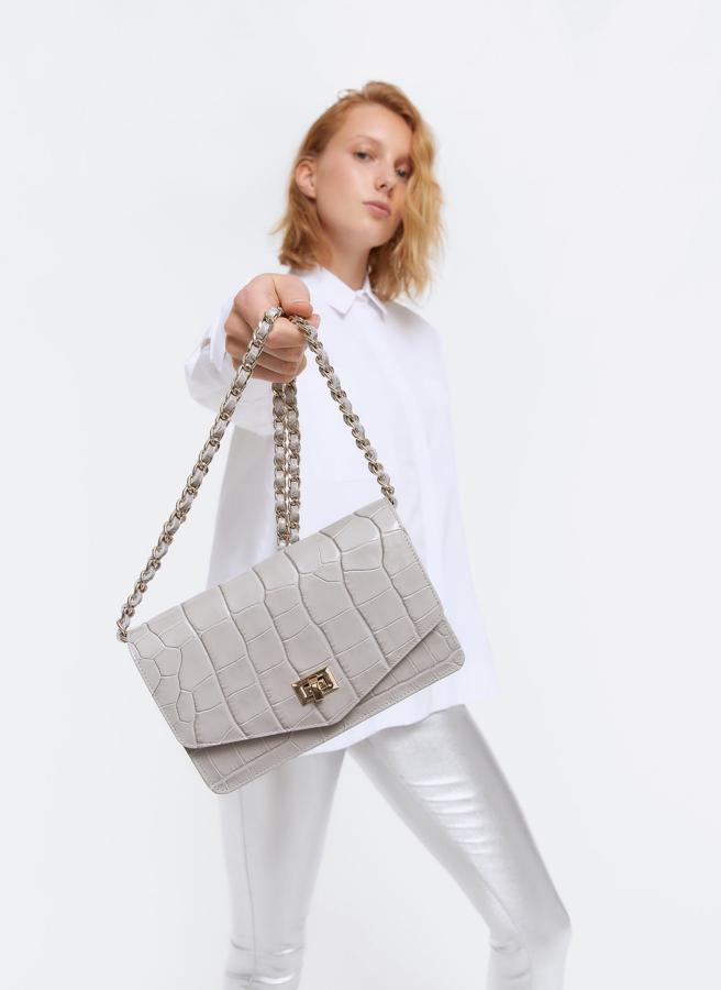 Uterqüe apuesta siempre por los clásicos y con este bolso gris en piel efecto cocodrilo y forma de sobre han acertado de pleno (99 euros).