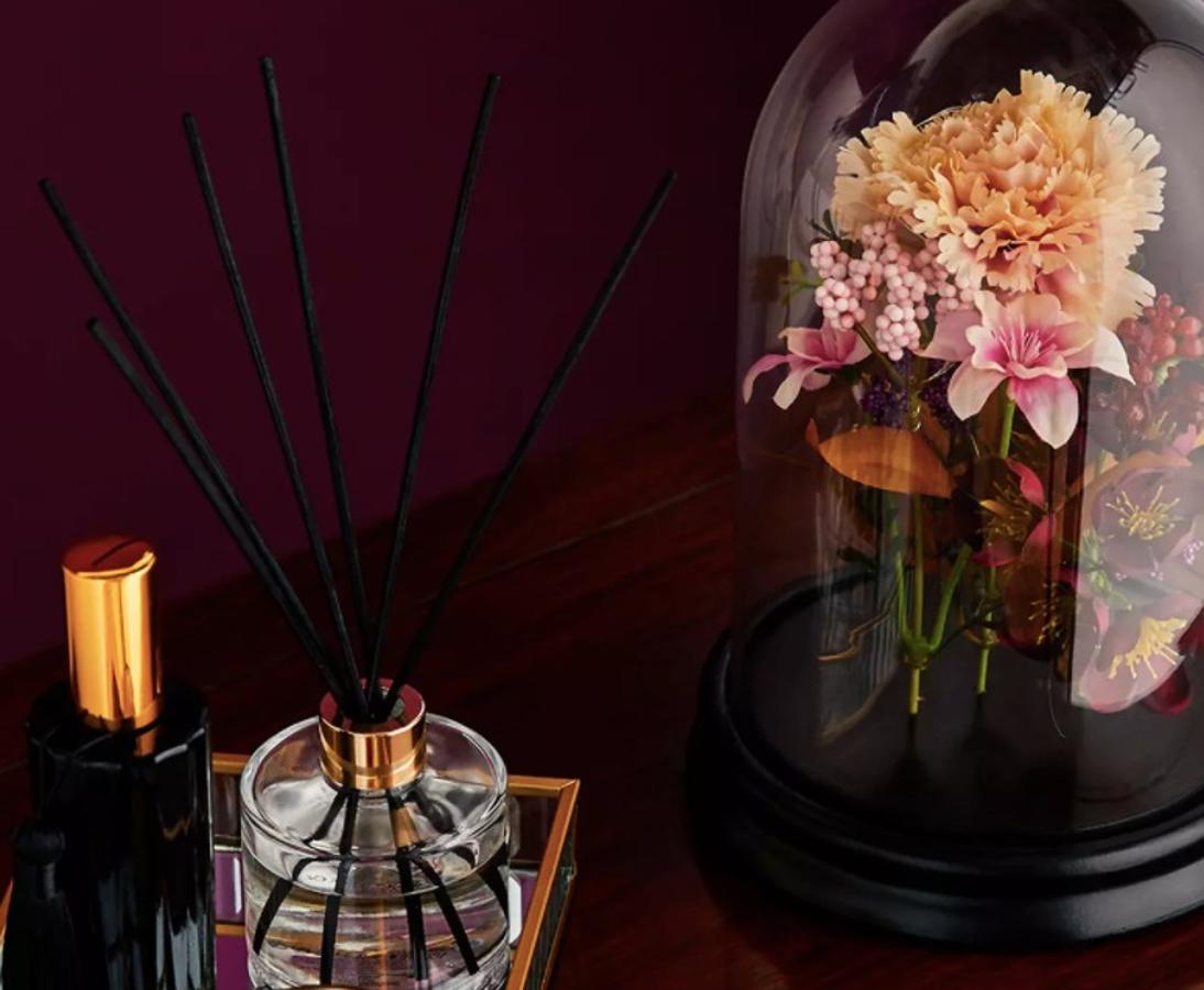 Pack de 2 bandejas de vidrio estriado 12 €, flores artificiales en campana de vidrio 7 €, aerosol doméstico «Midnight» 5 € y pack de 4 velas votivas doradas 7 €.