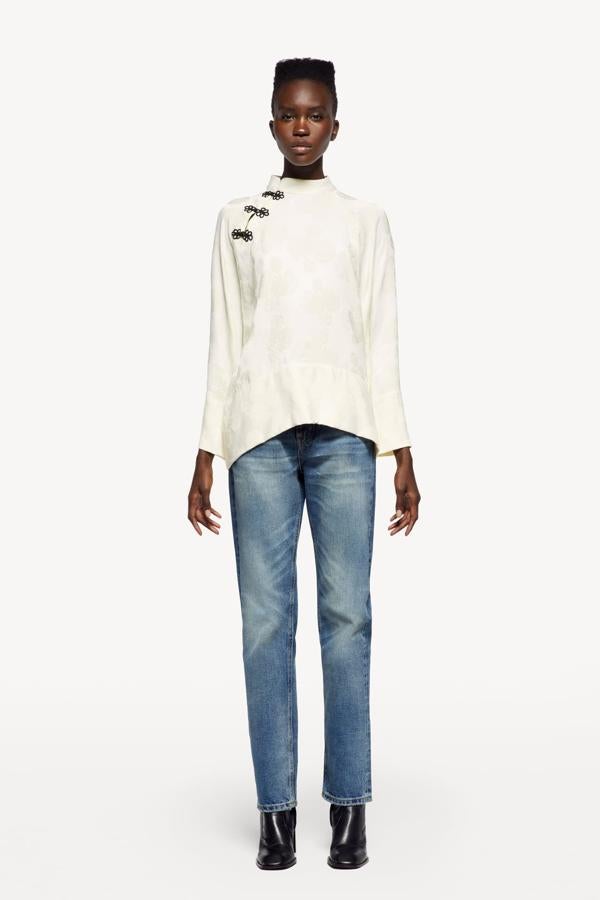 Blusa de cuello subido con manga larga amplia, bajo asimétrico y cierre frontal con alamares, de Zara (29,95 €).
