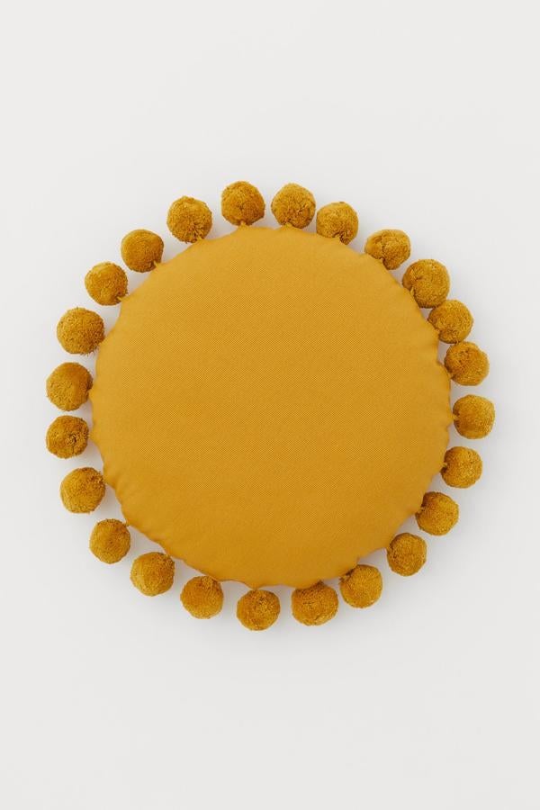 Todo parece indicar que vamos a pasar mucho tiempo en casa y la mejor forma de festejarlo es dando a nuestros ojos un festín de colores cálidos que llevan a nuestra vivienda la calidez y la luminosidad del sol. Un efecto que puedes lograr con piezas pequeñas, como este cojín redondo con pompones de H&M Home (29,99 euros).