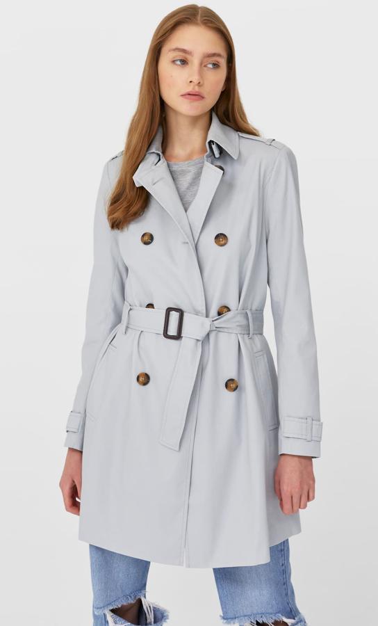 En color gris perla, este trench de botonadura cruzada y cinturón del mismo tejido cuenta con bolsillos frontales y tiene un precio de 29,99 euros.