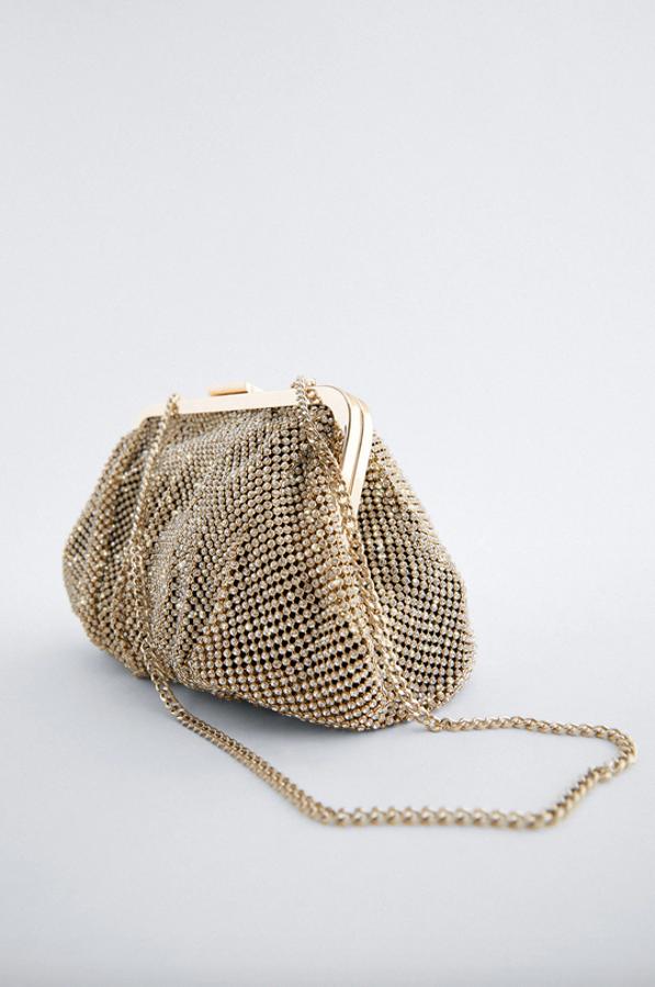 En color dorado y cuerpo con brillos, esta bandolera con boquilla metalizada, asa de hombro con cadena e interior forrado con bolsillo es de Zara y tiene un precio de 29,95 euros.