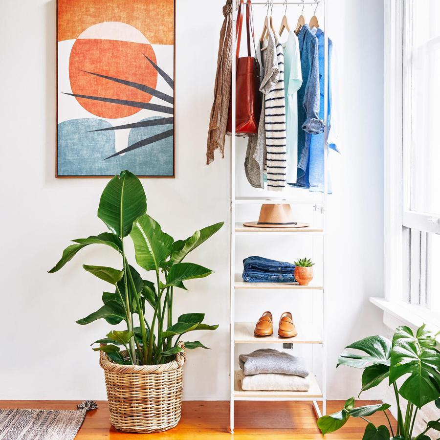 Cualquier rincón puede transformarse en un pequeño vestidor gracias a piezas tan versátiles como esta estantería (79 euros). Además, nos encanta la cesta (50 euros) a modo de macetero.