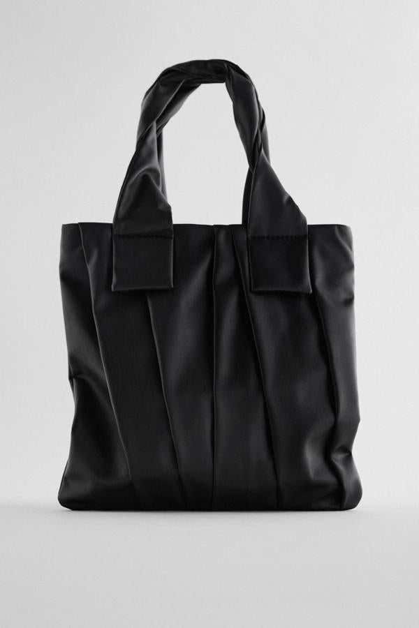 Este bolso formato shopper con cuerpo plano rectangular con pliegues cuenta con asas de hombro entrelazadas y cierre mediante cremallera. En color negro, es de Zara y tiene un precio de 25,95 euros.