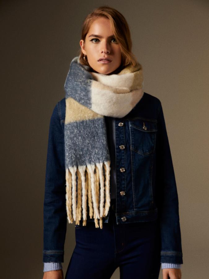 Con acabado de flecos a tonos combinados y tacto muy suave, esta bufanda con estampado de cuadros en blanco, beige y azul oscuro es de Lefties y tiene un precio de 12,99 euros.