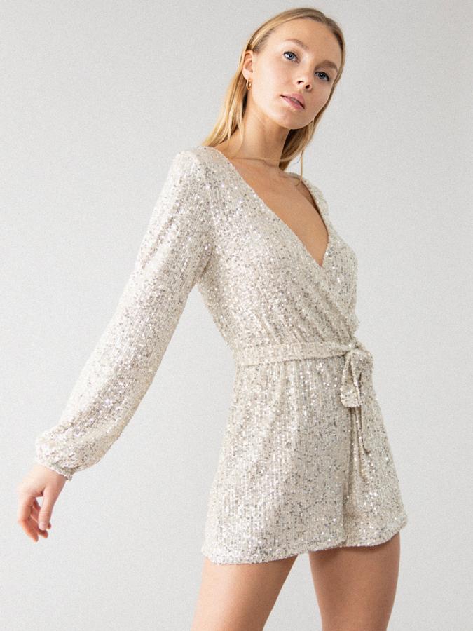 En plata, con mangas largas y escote de pico cruzado, este mono corto está confeccionado en tejido elástico de lentejuelas y viene con goma en la cintura con cinturón a tono. Tiene un precio de 22,99 euros y está disponible entre las tallas XS y XL.