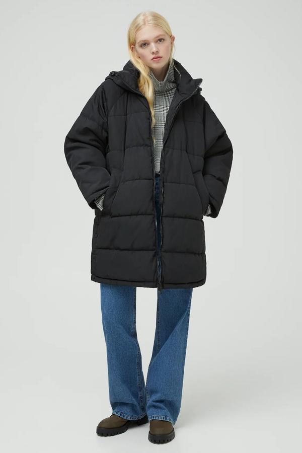 Disponible en negro o en crudo, este abrigo largo en tejido acolchado con capucha ajustable y cierre mediante cremallera es de Pull & Bear y tiene un precio de 49,99 euros.