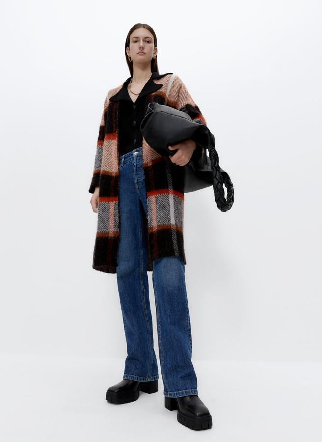 En punto jacquard y color negro con cuadros en naranja, este abrigo sin cuello ni cierre tiene un precio de 99 euros y está disponible entre las tallas S y M.