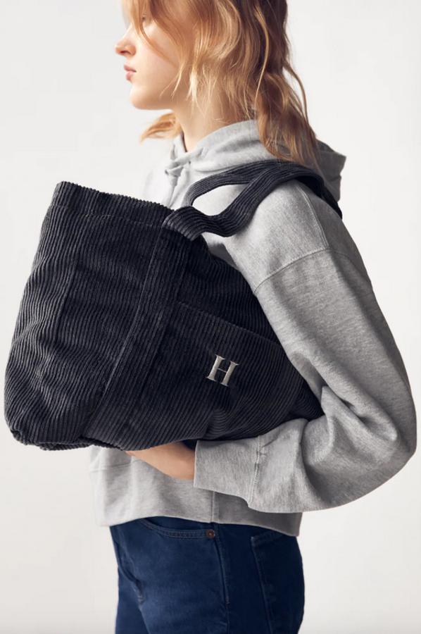 Formato shopper en gris oscuro para este bolso con cuerpo y asas de hombro en pana, interior forrado y cierre de cremallera metalizada de Zara. Cuesta 25,95 euros y podemos personalizarlo en seis colores diferentes por 3 euros más.