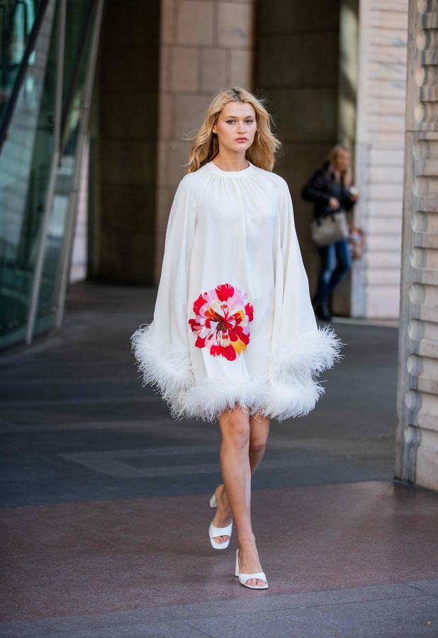 Vestido capa de raso blanco con flor bordada y plumas en el bajo.