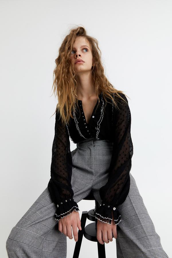 En Sfera hemos encontrado esta blusa de plumeti en color negro con chorreras y detalle de cuentas. Los puños tienen volantes y el cierre frontal es de botones metalizados. Tiene un precio de 19,99 euros y está disponible en las tallas S, M y L.