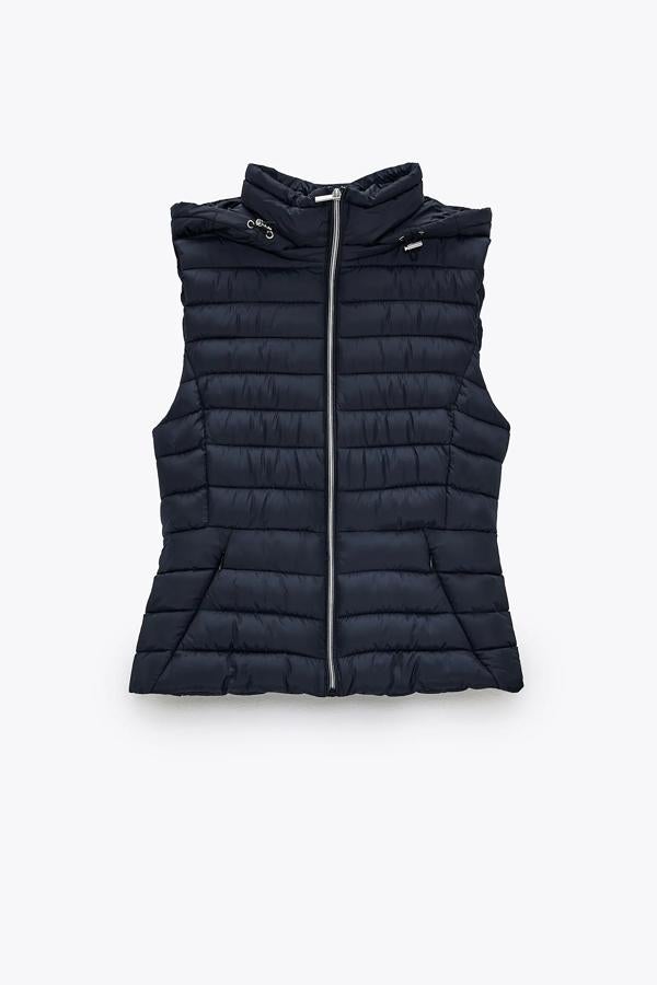 Este chaleco acolchado azul marino con diseño entallado cuenta con cuello subido con capucha y cierre frontal con cremallera metálica. Tiene un precio de 25,95 euros.