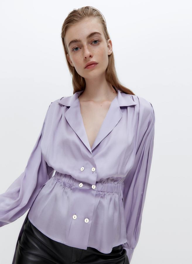 Confeccionada en un tejido satinado de alta calidad, esta camisa lila de Uterqüe viene con abertura mediante tapeta frontal cruzada doble con botones dorados, cintura elástica y cinturón a jugo y hombreras. Con cuello solapa, costaba 79 euros y ahora podemos comprarla por 49,95 euros en las tallas M y L.