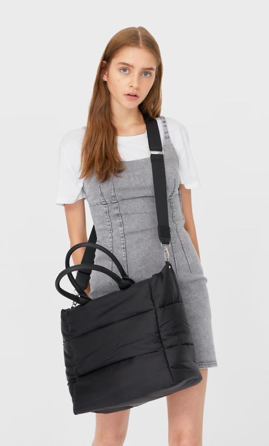 En color negro, con cremallera en el cuerpo acochado y asas de mano a tono en polipiel es de Stradivarius y viene también con asa de hombro con hebillas. Tiene un precio de 19,99 euros.