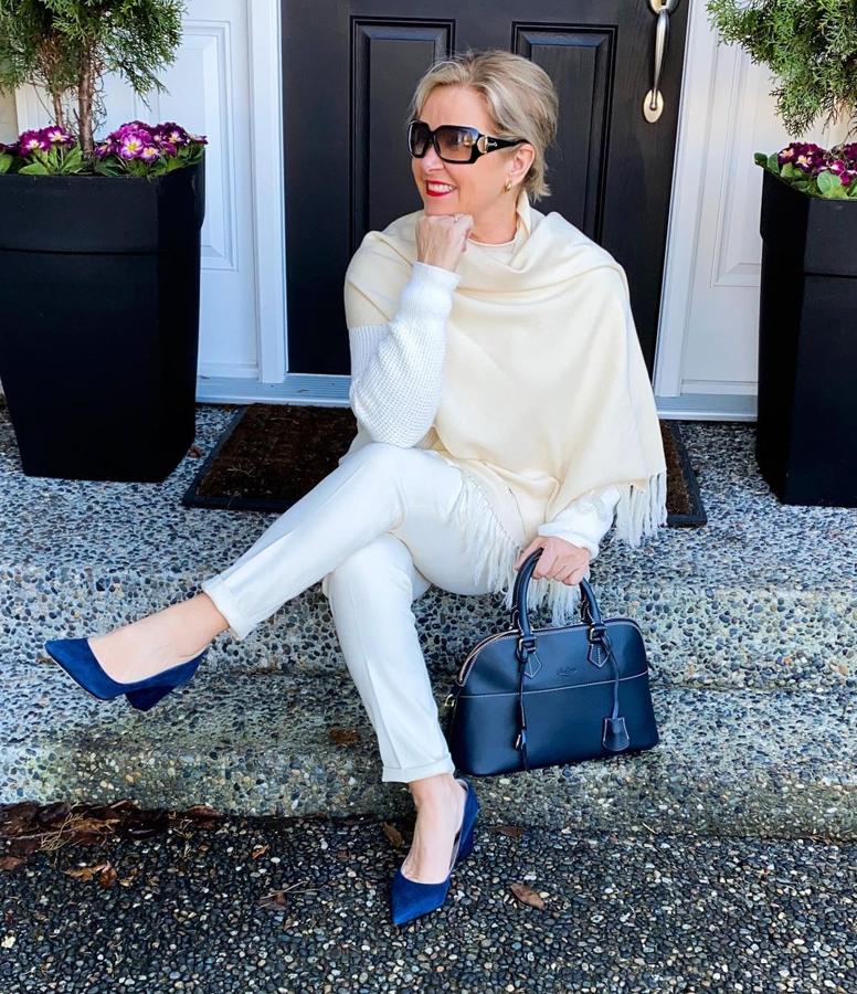 Woman over 50 wearing an all-white casual outfit with navy shoes and handbag.