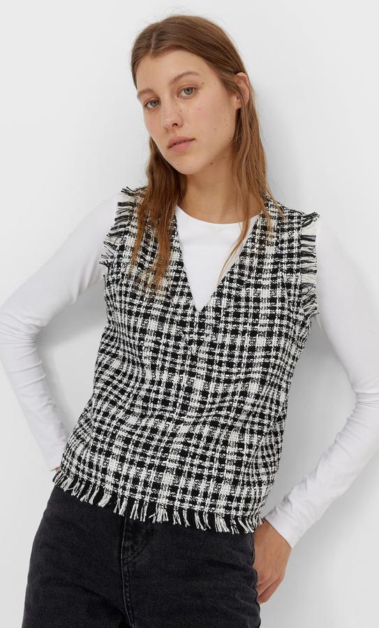 En blanco y negro con estampado de cuadros, este chaleco con cuello de pico y manga sisa desflecada, al igual que el bajo, tiene un precio de 17,99 euros y está disponible entre las tallas XS y XL.