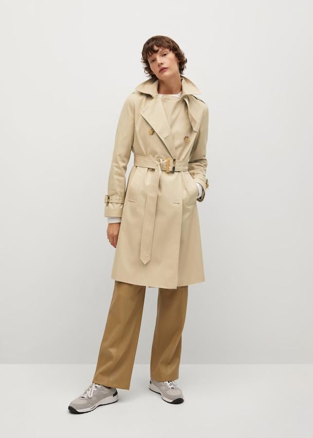 Trench cruzado de algodón con tratamiento repelente al agua, cuello de solapa, manga larga con puños abotonados, trabillas, cinturón ajustable, bolsillos laterales y cierre de botones en la parte delantera, de Mango (59,99 €).