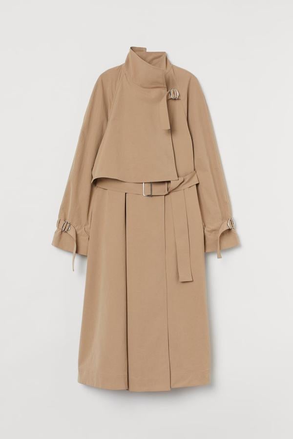 Gabardina midi de tela con cuello elevado y canesú suelto en la parte superior con trabilla y hebilla de metal, mangas raglán amplias con trabilla y hebilla de metal en los puños, bolsillos en las costuras laterales, cinturón ancho con hebilla de metal y bajo con vuelo, de H&M (69,99 €).