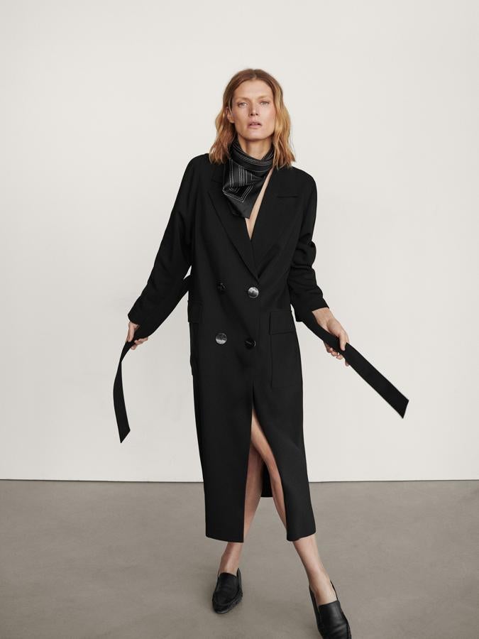 De corte recto, con cuello de pico con solapas y cierre cruzado mediante doble botonadura, este abrigo trench en crepé negro viene con cinturón de lazada a tono y abertura en el bajo en la parte posterior. Podemos encontrarlo en las tallas S, M y L por 169 euros.
