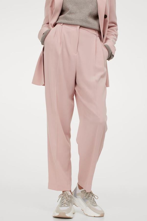 De venta exclusiva en la web de H&M, este pantalón en rosa claro de diseño tobillero con pinzas viene con talle alto con cierre cremallera y corchete, perneras pitillo con raya y bolsillos al bies. Está confeccionado con poliéster parcialmente reciclado, tiene un precio de 29,99 euros y está disponible entre las tallas 32 y 50.