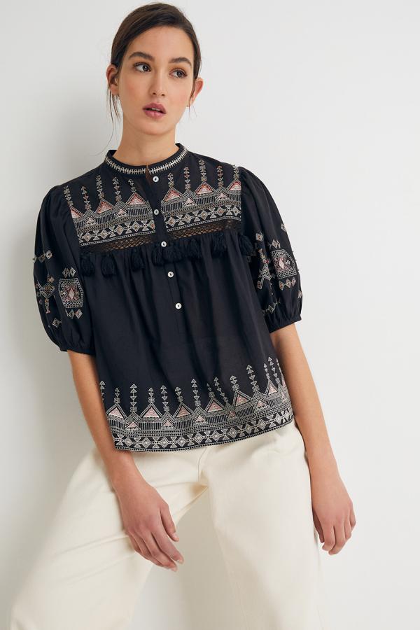 En color negro y de manga corta abullonada, esta blusa con bordados en tonos tierra cuenta con botones en la parte delantera y tiene un precio de 25,99 euros.