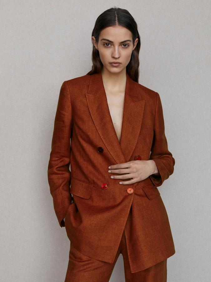 En un bonito e intenso color terracota, esta americana con cuello con solapa de pico, cierre cruzado mediante doble botonadura frontal a tono y dos bolsillos laterales con solapa viene con abertura en la parte posterior y pantalón a juego. Podemos encontrarla entre las tallas 34 y 44 por 129 euros.