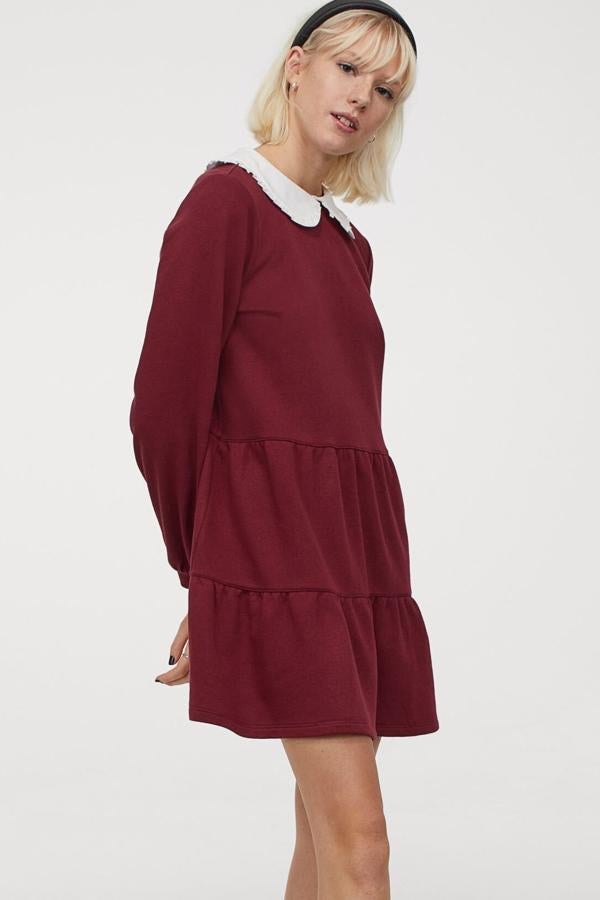 Disponible en gris o en rojo oscuro, este vestido en tejido de sudadera con cuello con ribete de volantes y falda con fruncido escalonado y vuelo tiene un precio de 29,99 euros. Es de H&M.