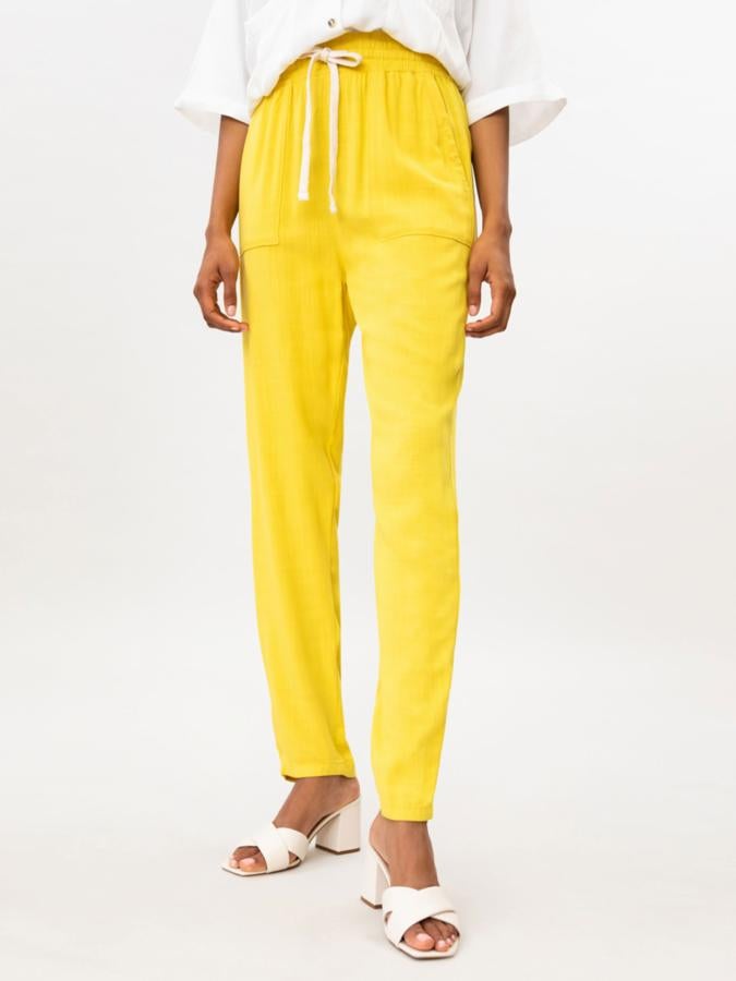 En color amarillo y disponible también en negro y beige, este pantalón fluido con cintura elástica con cordón cuenta con bolsillos laterales y tiene un precio de 12,99 euros.