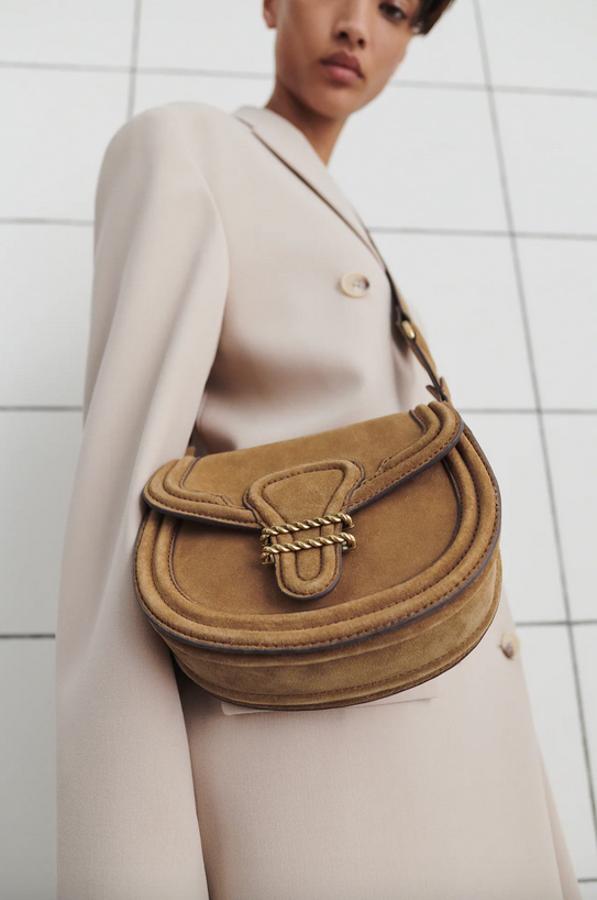 Confeccionada con piel curtida sostenible, esta bandolera de Zara en color marrón con cuerpo ovalado y detalles metalizados en el cierre de la solapa, viene con asa de hombro ajustable y extraíble y cierre mediante imán. Cuesta 49,95 euros.