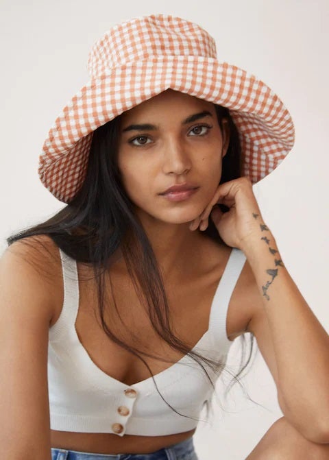 Que no falte un gorro bucket en tu armario con el estampado vichy de la temporada. Este es de Mango y su color naranja va a elevar el nivel de cualquier look básico. (15,99 euros).