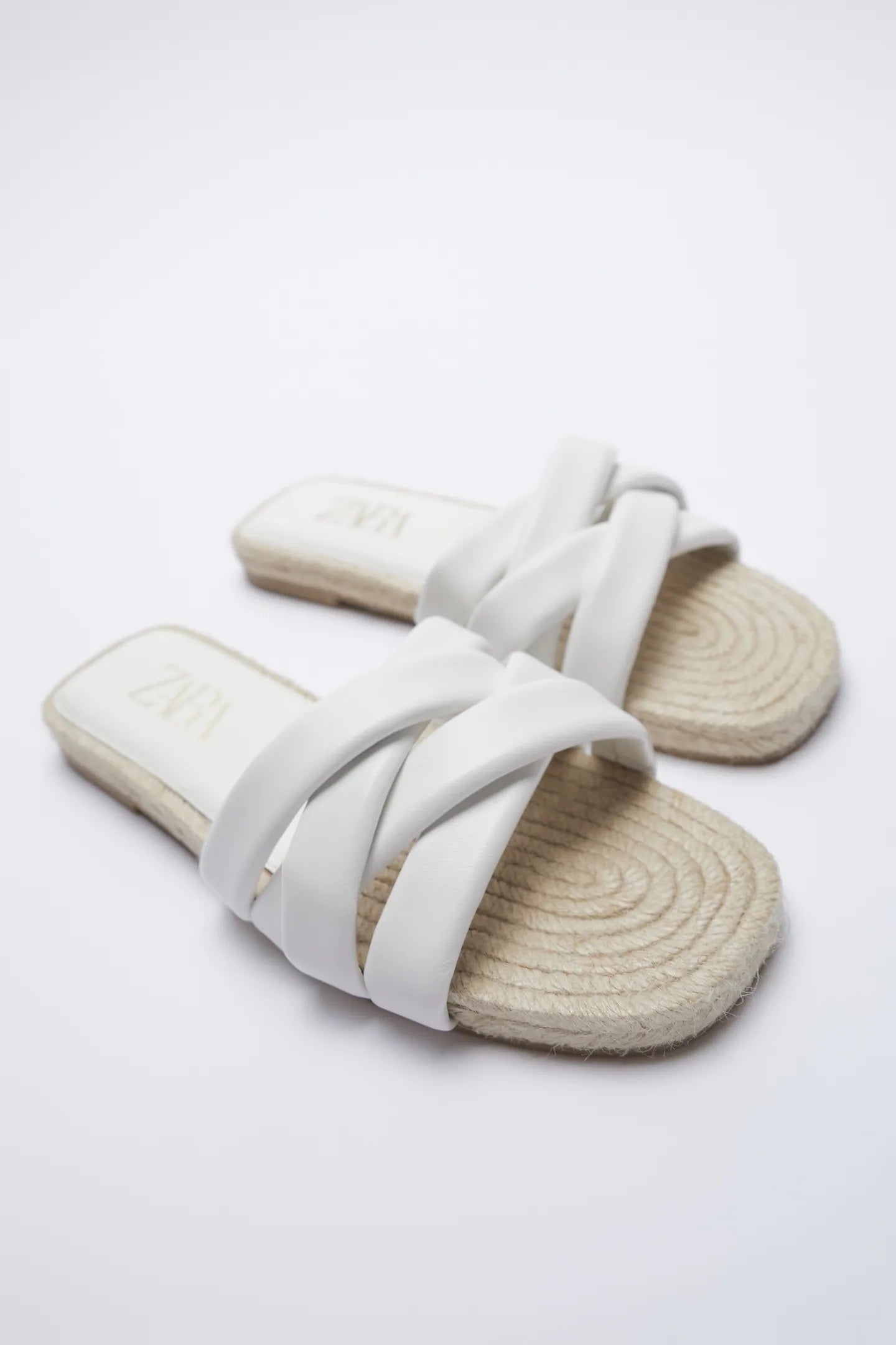 Sandalias planas de Zara con tiras blancas cruzadas y acolchadas y suela cuadrada de yute. Ideales para llevar 24/7 incluso para estar por casa. (29,95 euros).