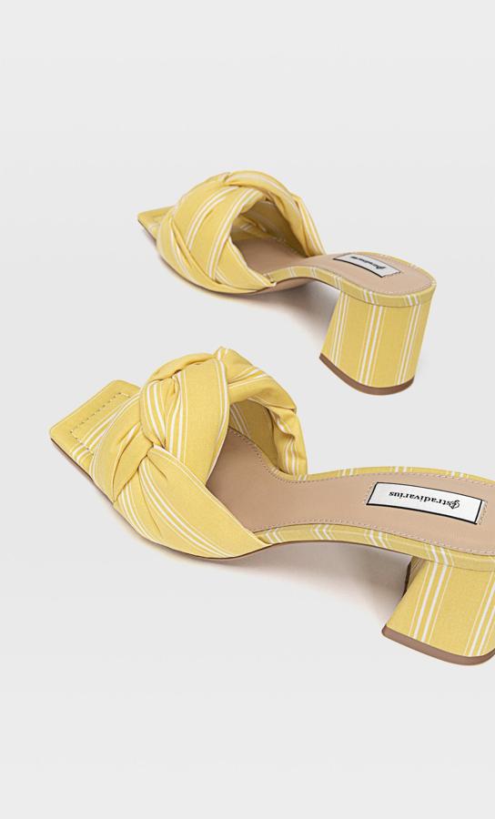 Estas sandalias de tacón forradas de tejido en color amarillo y detalle de nudo en la parte superior tienen un precio de 29,99 euros.