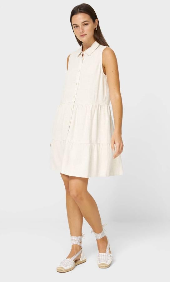 Este vestido camisero de cuello solapa y manga sisa en color piedra cuenta con cierre de botones en la parte delantera y bajo acabado en volantes. Tiene un precio de 15,99 euros.