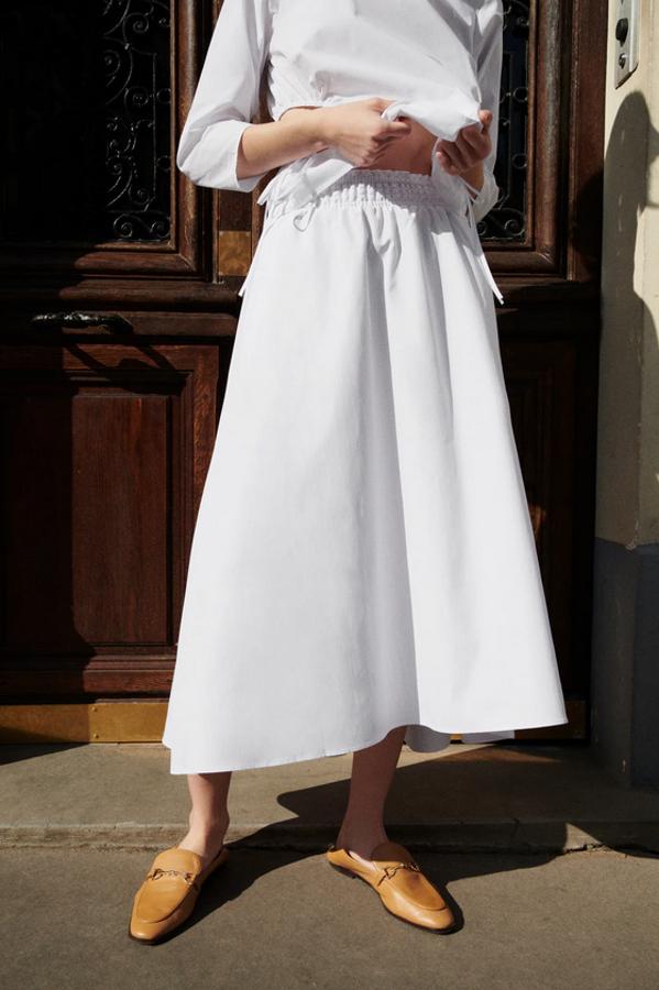 De tiro alto, con cintura elástica y bolsillos laterales ocultos en costura, esta falda blanca de popelín es de Zara y viene con el bajo acabado en evasé. Disponible entre las tallas XS y XL, cuesta 25,95 euros.