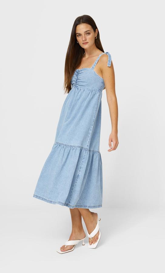 En denim claro, con escote recto con elástico y tirantes regulables con lazada, este vestido largo de Stradivarius viene con el bajo acabado en volante amplio. Está disponible entre las tallas XS y XL por 29,99 euros.