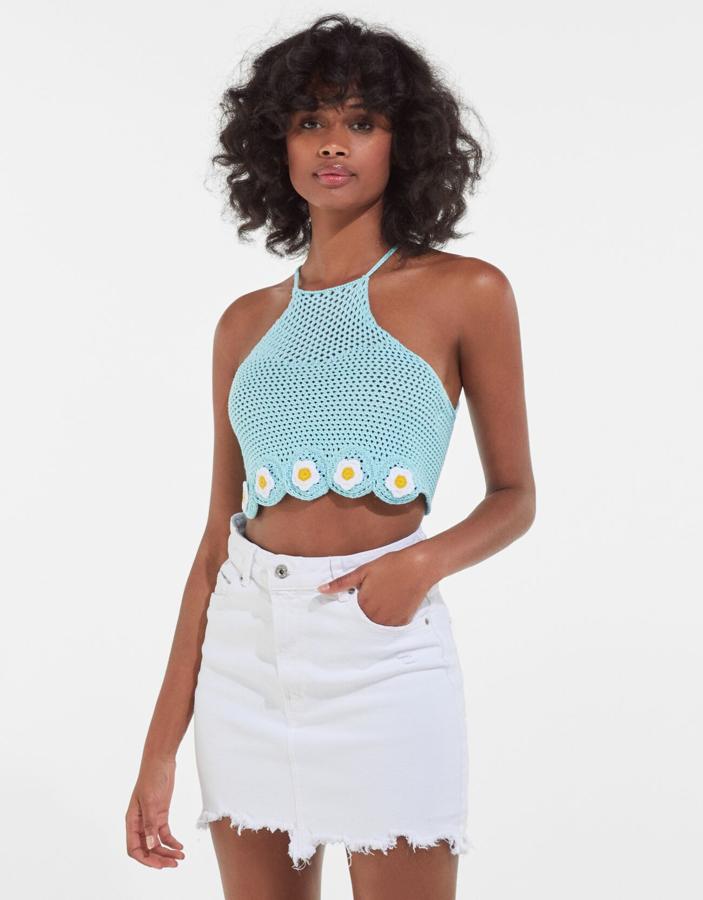 En azul pastel, con bajo de flores en blanco y amarillo, este top crochet de Bershka con cuello halter y tiras cruzadas en la espalda cuesta 15,99 euros y está disponible entre las tallas XS y L.
