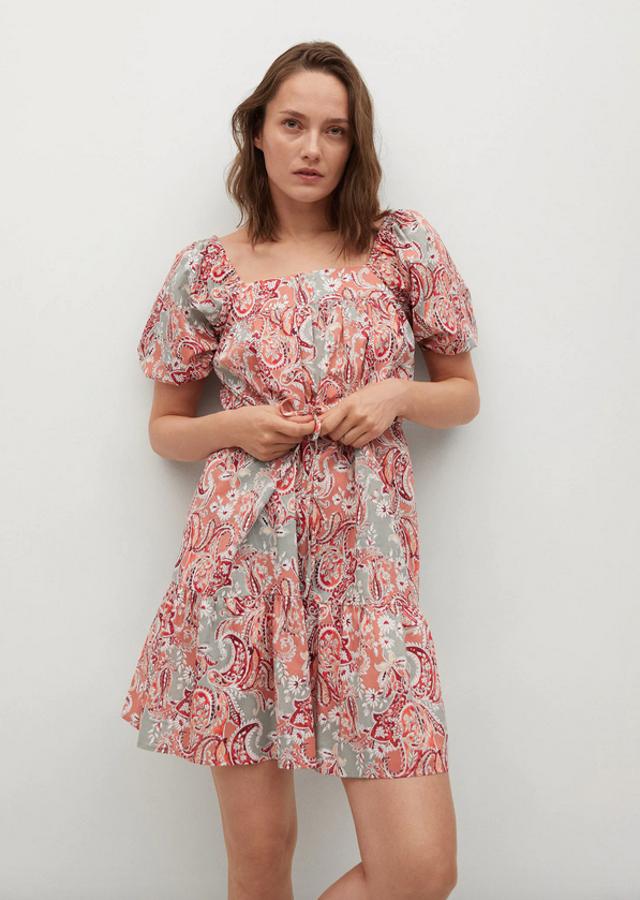 Estampado paisley en rojo, salmón y gris para este vestido de Mango de diseño corto acampanado, escote recto y mangas cortas abullonadas acabadas en puños elásticos. Con cinturón ajustable y volante en el bajo, viene con detalles plisados y podemos encontrarlo entre las tallas XS y XL por 25,99 euros.