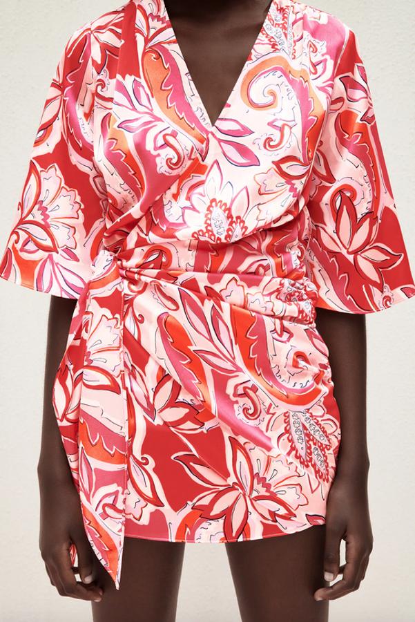 Con escote de pico y mangas amplias por debajo del codo, este vestido corto con detalle de pliegues laterales, cierre interior con botones y diseño tipo pareo con lazada en color rojo y blanco es de Zara y cuesta 29,95 euros. Podemos encontrarlo entre las tallas XS y XXL.
